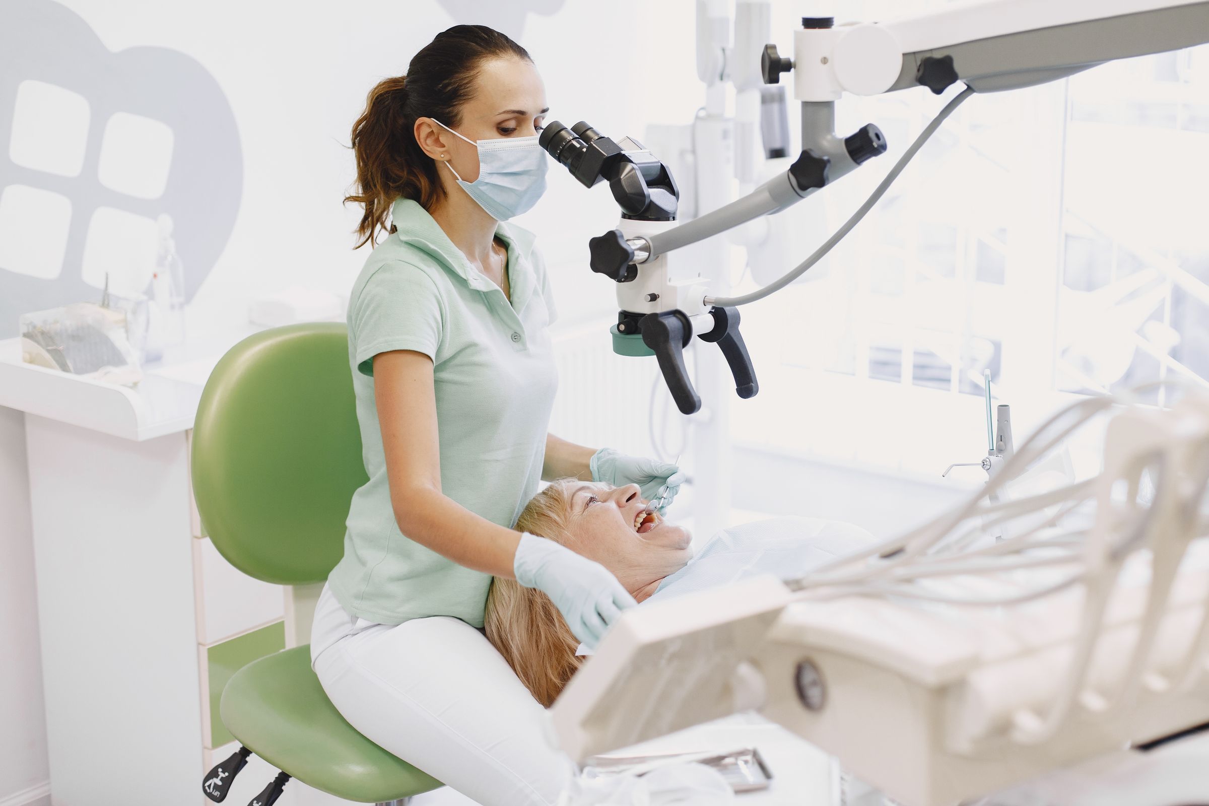 A dentist works with a microscope on a smiling patient