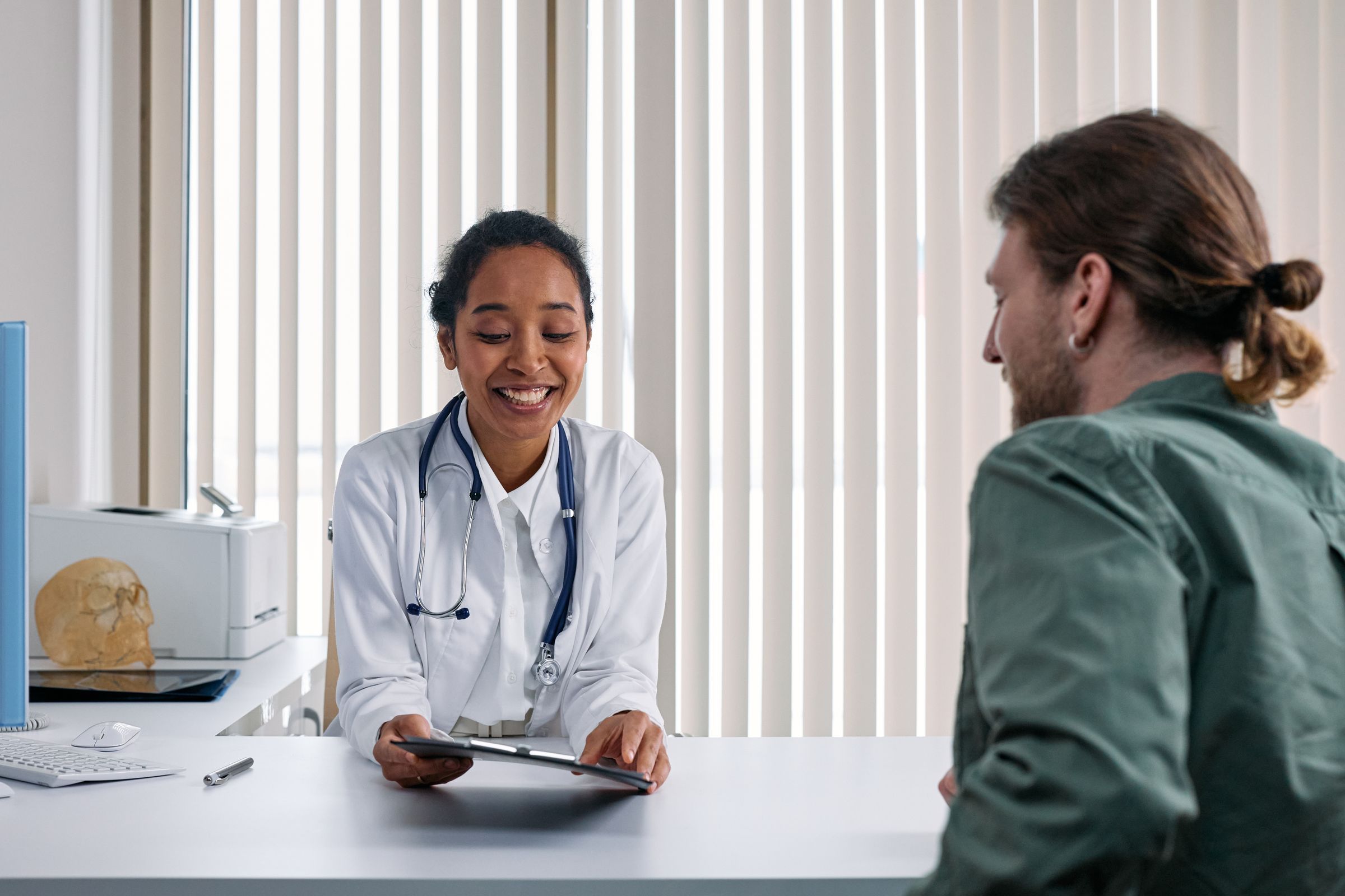 A smiling GP talks a patient through something on her tablet at a consult desk